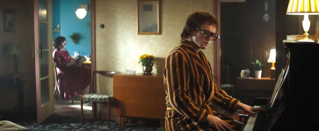 Taron Egerton as Elton John playing piano in his parents house in Rocketman