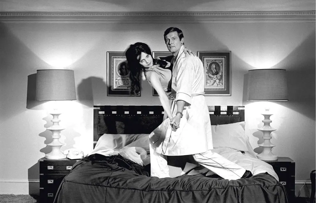 Roger Moore as James Bond and Madeline Smith as Miss Caruso posing on bed on the film set of 'Live and Let Die', 1973
