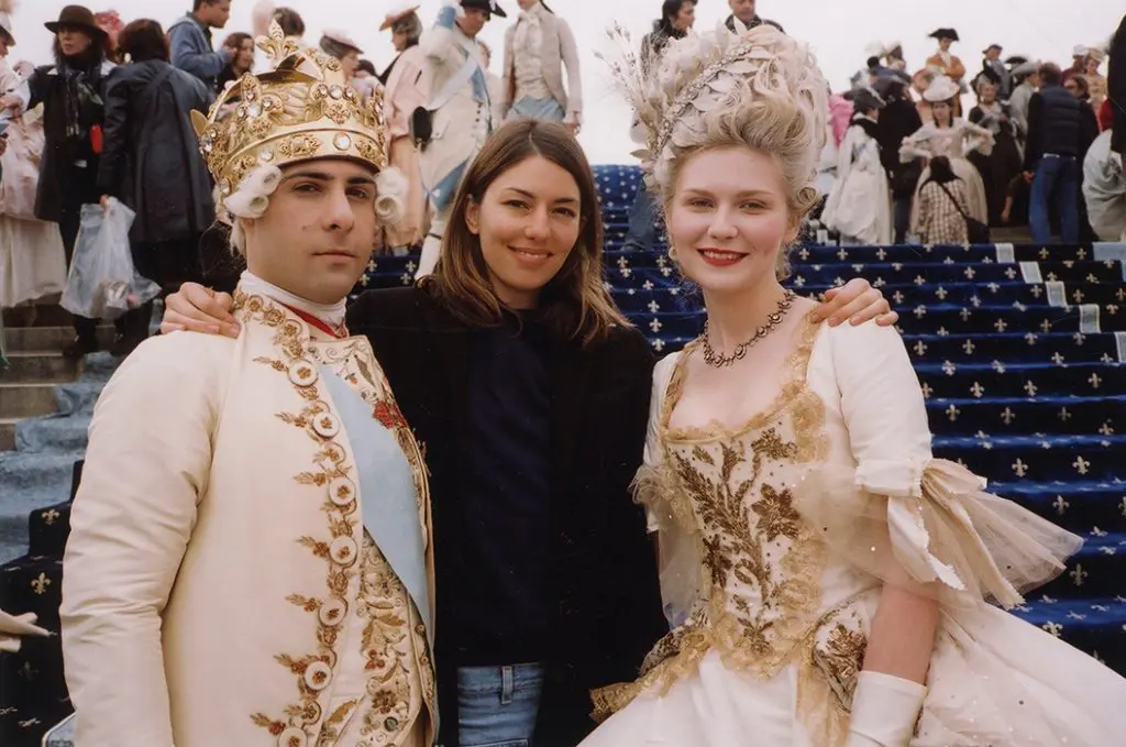 Sofia Coppola on the set of Marie Antoinette, flanked by Jason Schwartzman as Louis XVI and Kirsten Dunst as Marie Antoinette, resplendent in their royal costumes.