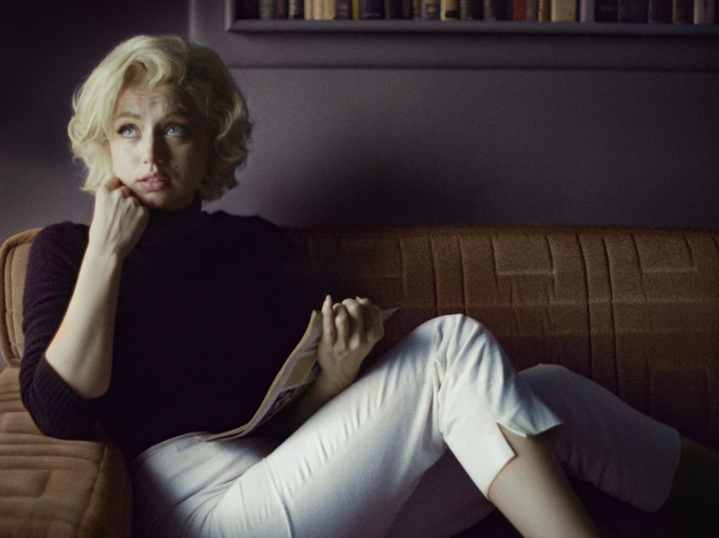 Blonde De-armas reenacting Marilyn Monroe on brown sofa chair